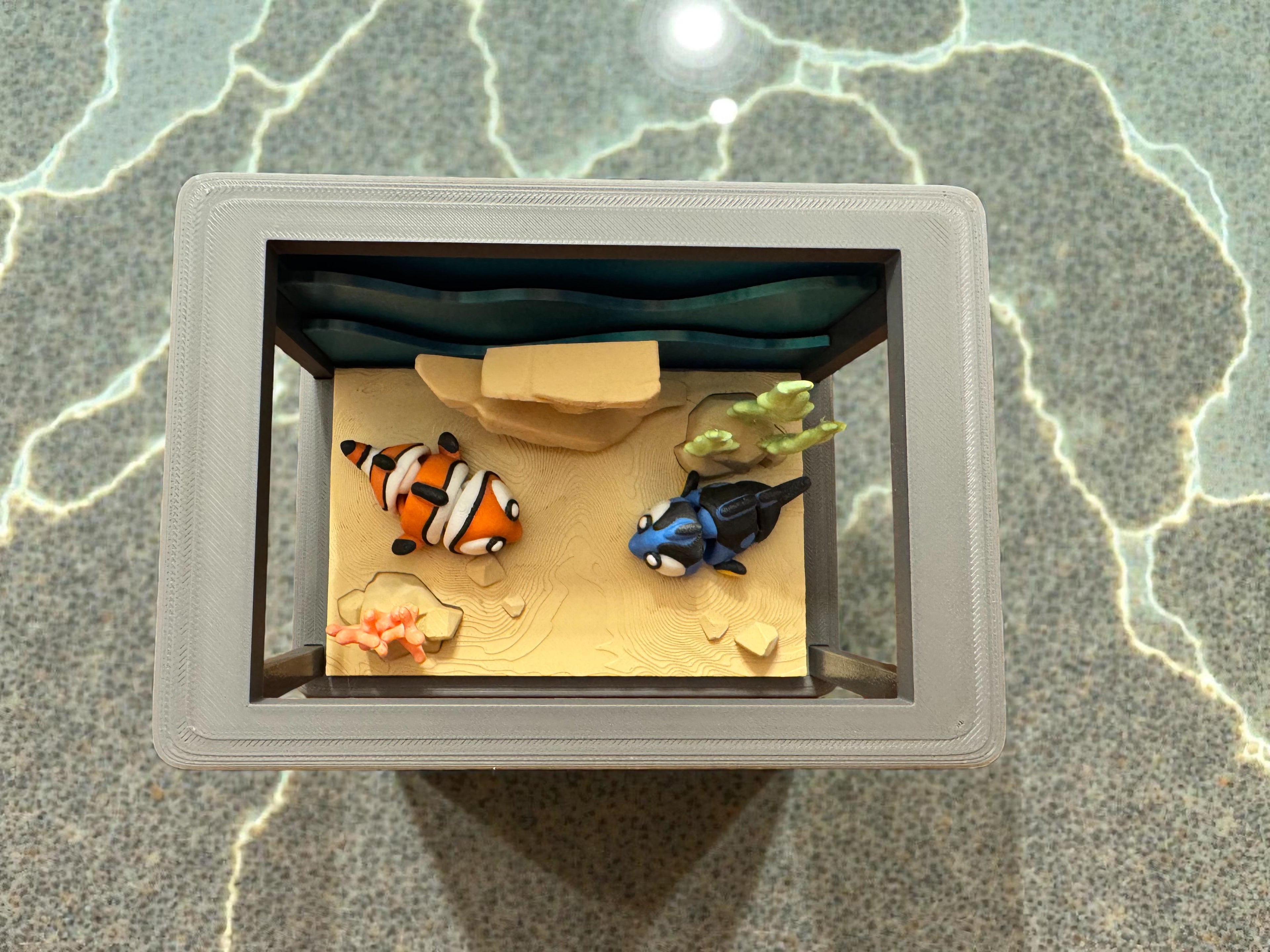 Model of a fish tank with two fish inside on a textured surface