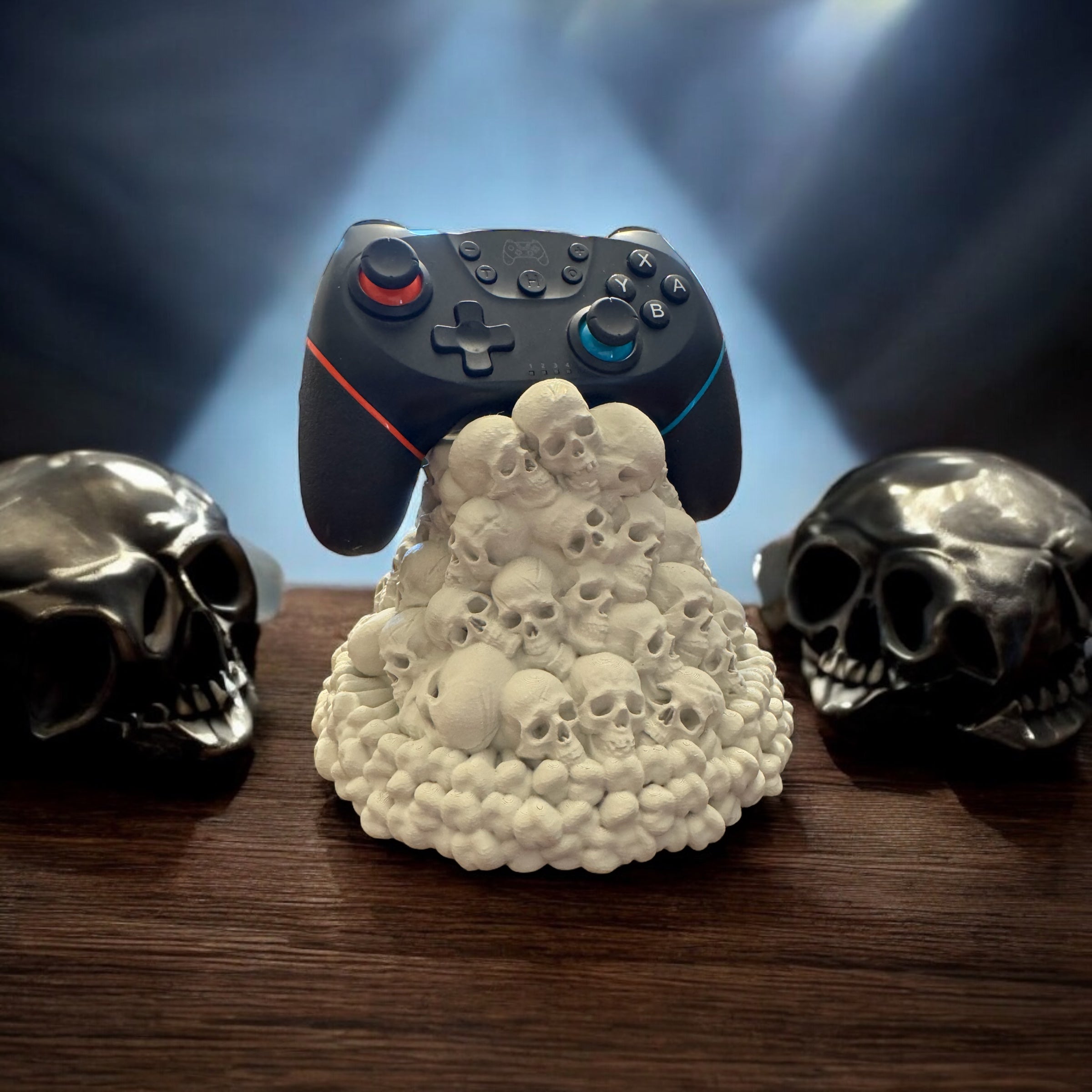 Gaming controller on a skull-shaped stand with two skulls on either side, against a dark background.